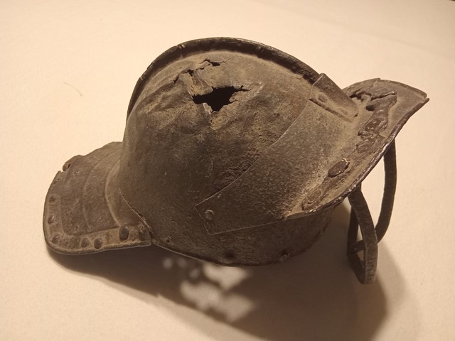 Family lore holds that the iron ‘lobster pot’ helmet pictured here was worn by Alexander Cosby on the grim day in 1596 when he and his son Francis were killed by the O'Mores in a skirmish in Stradbally. There is also a suggestion that it was worn by Richard Cosby, a generation later when he challenged the O’Mores to a pitched battle in the Glyn of Aughnahelly below the Rock of Dunamase in 1608.  In truth, the helmet is more likely to have been worn during the Confederate Wars, part of the War of the Three Kingdoms (1639-1653). The three bars formed a cage visor at the front, affording a degree of protection while allowing the wearer to see and breathe. The brim at the back provided additional protection to the neck, shielding it from potential strikes or projectiles from behind. Both the visor and the brim were also designed to channel rainwater away from the face, which could make all the difference to the wearer during combat.