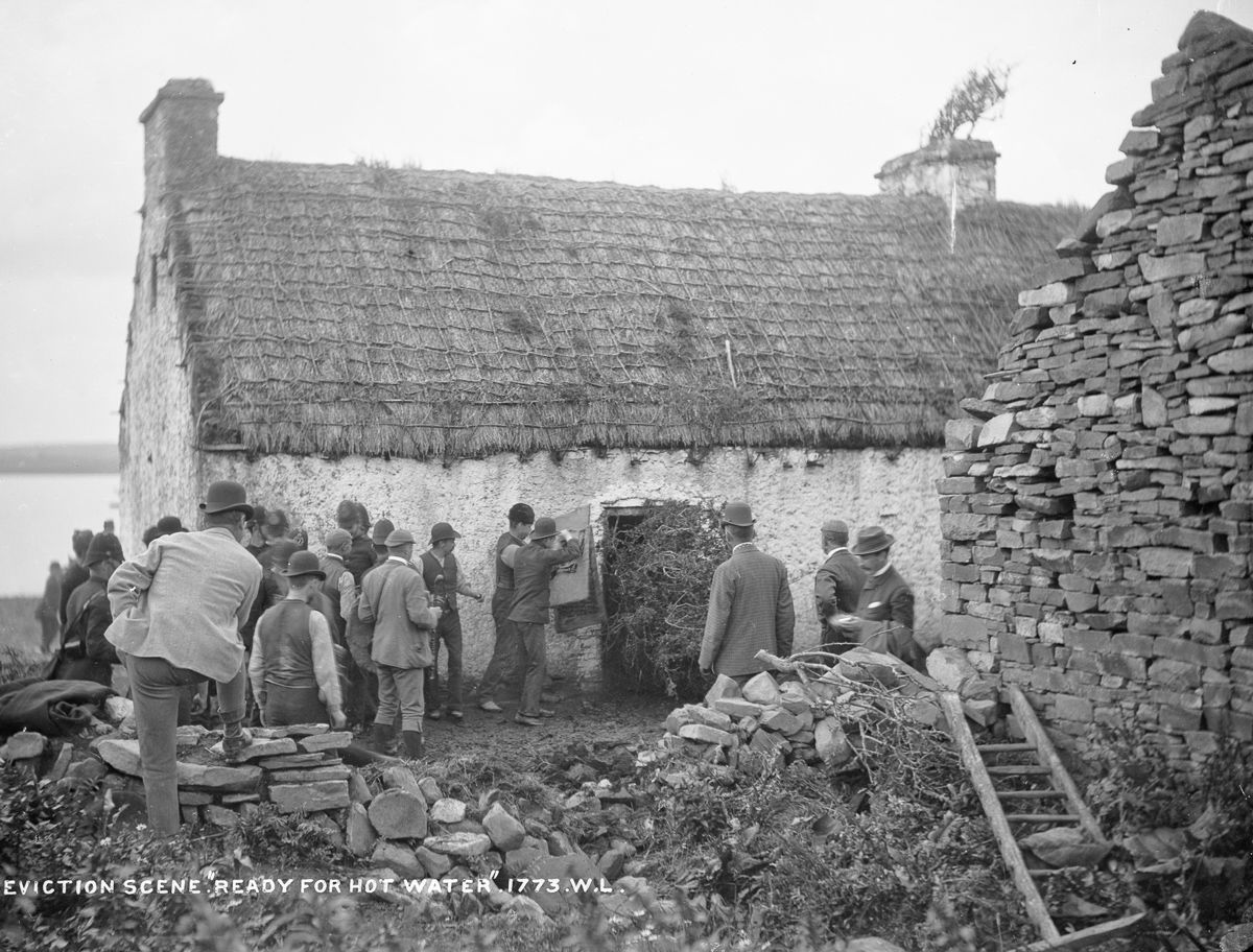 Eviction scene, Vandeleur Estate, County Clare, c. 1880–1900. Men prepare to force entry into a thatched cottage during an eviction, while defenders gather nearby; the original caption, “Ready for Hot Water,” refers to resistance anticipated from within the house. Photograph from the Lawrence Collection, attributed to Robert French.
